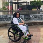 Abha out somewhere sitting in her wheelchair wearing white attire and smiling