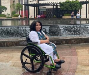 Abha out somewhere sitting in her wheelchair wearing white attire and smiling